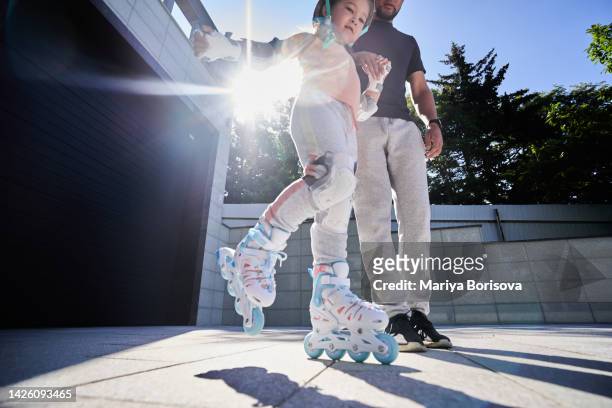 a father teaches his daughter to rollerblade in the rays of the sun. - kneepad stock pictures, royalty-free photos & images