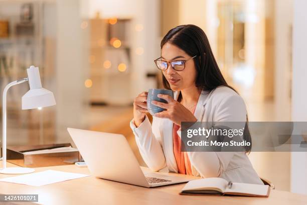 mujer en el escritorio, en la oficina con café o té y computadora portátil, revisando el correo electrónico o el proyecto. mujer profesional en el trabajo, usando una computadora portátil, para analizar negocios o leer informes en un contexto bokeh. - acontecimientos en las noticias fotografías e imágenes de stock