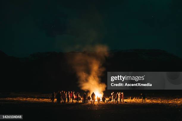distant view of people gathered around a fire at night - camp fire stock pictures, royalty-free photos & images