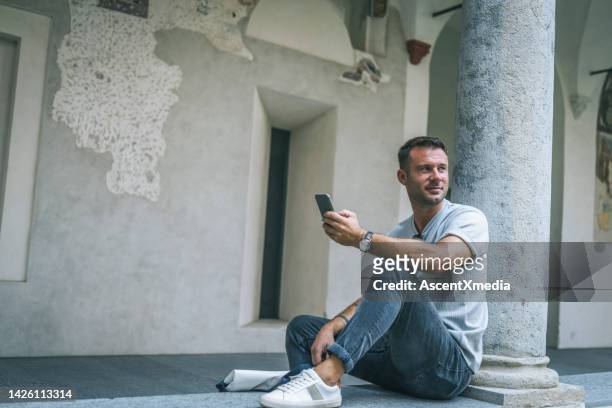 man uses phone in courtyard - rolled up pants stockfoto's en -beelden