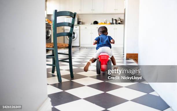 little boy riding his toy tricycle in a kitchen - toddler toys stock pictures, royalty-free photos & images