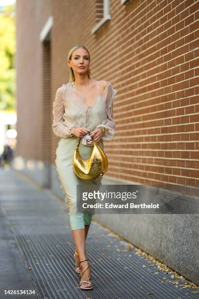 Leonie Hanne wears gold large earrings from Fendi, a beige silk V-neck / long sleeves / midi dress, a pale green silk V-neck / midi dress, a gold...