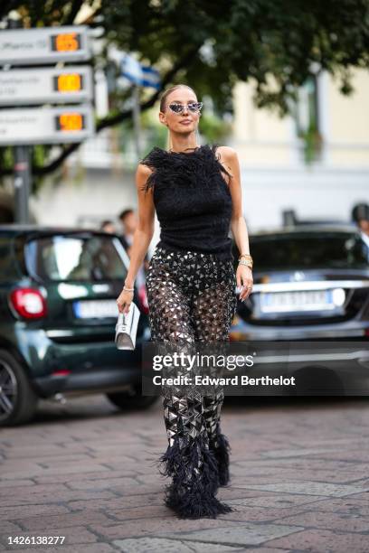 Leonie Hanne wears silver and rhinestones cat eyes sunglasses, rhinestones and black fringed earrings, a black feathers neck / sleeveless tank-top, a...