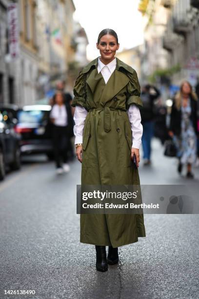 Olivia Palermo wears a white shirt, a khaki puffy shirt sleeves / long belted coat, black shiny leather pointed heels ankle boots, outside Alberta...