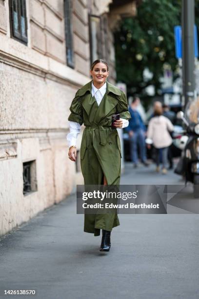 Olivia Palermo wears a white shirt, a khaki puffy shirt sleeves / long belted coat, black shiny leather pointed heels ankle boots, outside Alberta...