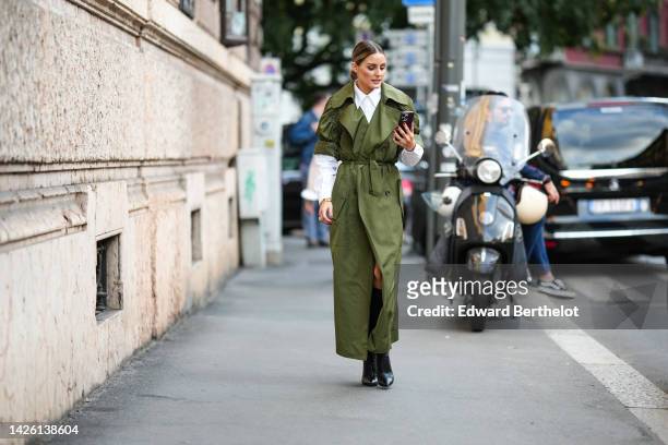Olivia Palermo wears a white shirt, a khaki puffy shirt sleeves / long belted coat, black shiny leather pointed heels ankle boots, outside Alberta...