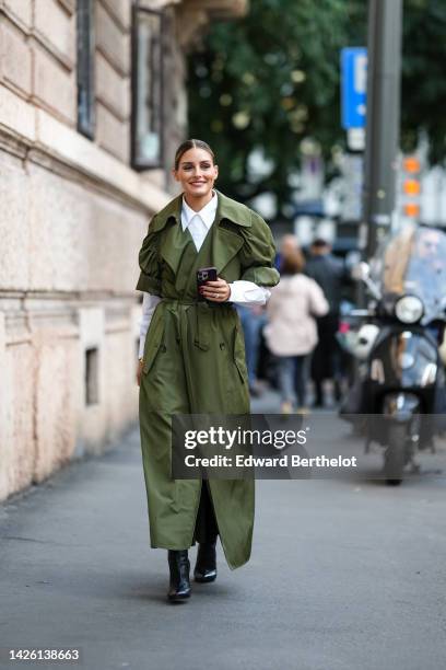 Olivia Palermo wears a white shirt, a khaki puffy shirt sleeves / long belted coat, black shiny leather pointed heels ankle boots, outside Alberta...