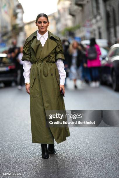 Olivia Palermo wears a white shirt, a khaki puffy shirt sleeves / long belted coat, black shiny leather pointed heels ankle boots, outside Alberta...
