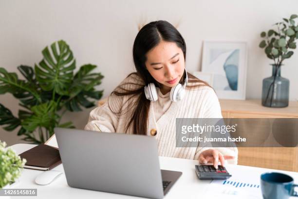 beautiful young woman calculating taxes to be paid while working from home with laptop. - planeamento financeiro - fotografias e filmes do acervo
