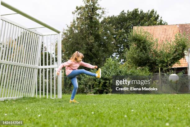 the girl stands at the gate and hits the soccer ball with her foot. children play football and various outdoor and active games - kicking stock-fotos und bilder