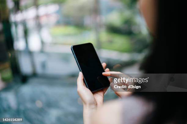 over the shoulder view of young asian businesswoman using smartphone. female executive is touching the display screen of her mobile phone in office - アクセス ストックフォトと画像