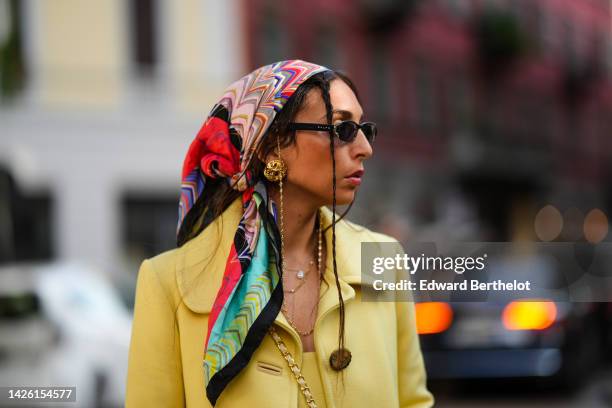 Gabriella Berdugo wears a red / blue / white print pattern silk scarf on the head, black sunglasses, silver earrings, gold necklaces, a yellow...