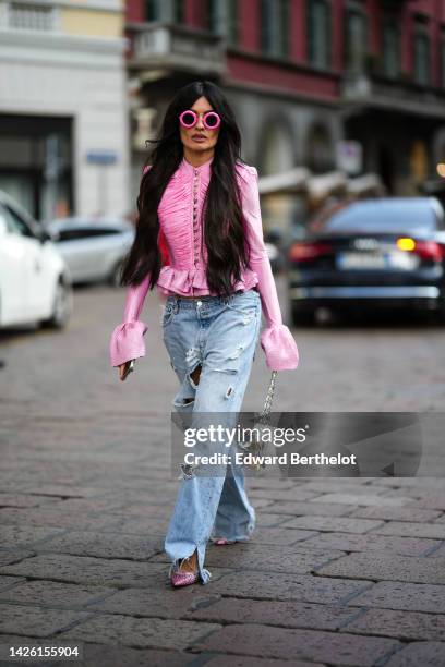 Angela Rozas Saiz wears pink circle sunglasses, a pink embossed ruffled long flared sleeves / silver buttoned top, blue faded denim ripped large...