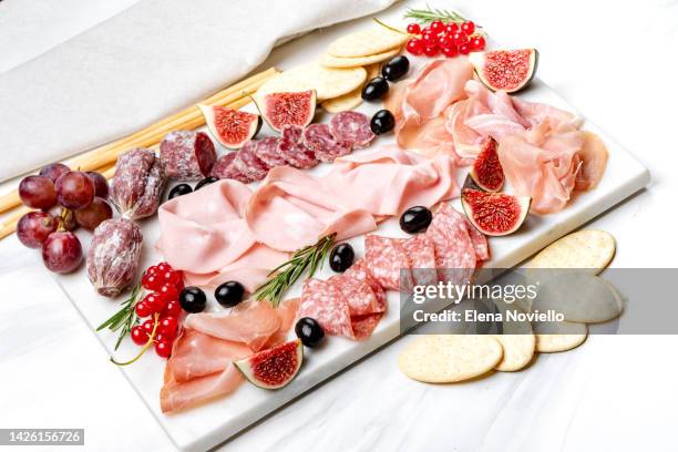 сharcuterie board with salami and prosciutto served with olives and grapes. snacks in the restaurant for an aperitif or a family dinner - charcuterie stockfoto's en -beelden