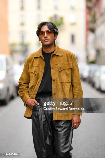 Rahi Chadda wears brown sunglasses, a black t-shirt, a yellow mustard suede jacket, black shiny leather puffy pants, outside Alberta Ferretti ,...