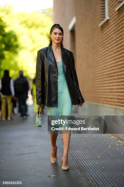 Brittany Xavier wears gold pendant keys earrings, a gold and diamonds necklace from Fendi, a black shiny leather blazer jacket, a pale green silk...