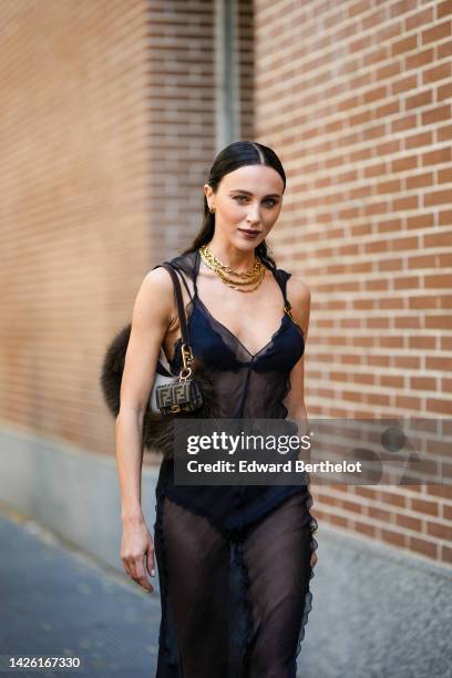 Mary Leest wears gold earrings, gold large chain necklaces, a black silk ruffled V-neck / tank-top / transparent midi dress from Fendi, a brown fur...