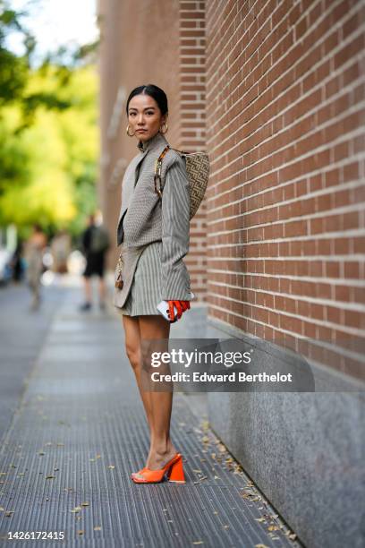 Yoyo Cao wears gold large earrings, a black and white small checkered print pattern high neck / long sleeves / wrap jacket from Fendi, a matching...