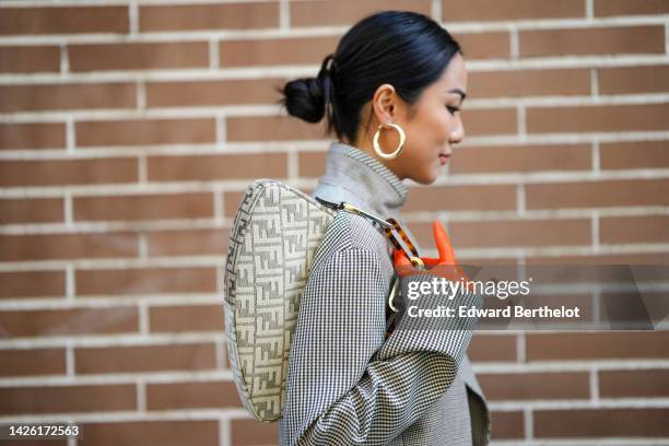 Yoyo Cao wears gold large earrings, a black and white small checkered print pattern high neck / long sleeves / wrap jacket from Fendi, a matching...