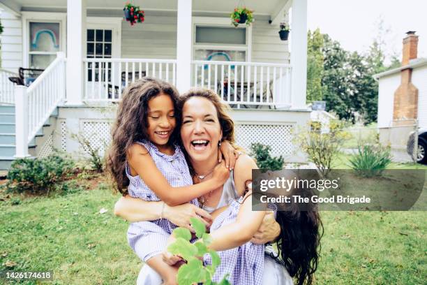 portrait of cheerful mother embracing daughters in front of house - family in front of home fotografías e imágenes de stock