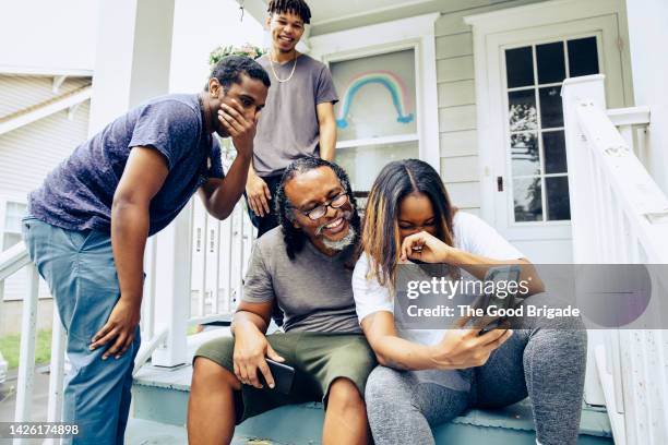 young woman laughing while taking selfie with father and brothers at porch - awkward family photo stock pictures, royalty-free photos & images
