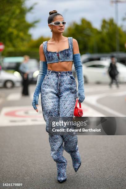Thassia Naves wears silver sunglasses from Prada, silver earrings, a blue faded denim square neck / cropped tank-top, blue fade denim high mittens,...