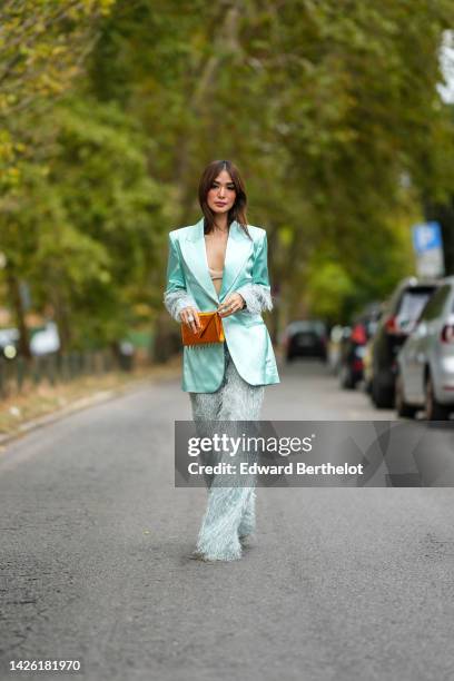 Heart Evangelista wears earrings, a beige bra underwear, a min green blue shiny silk with embroidered feathers sleeves jacket from Collini, matching...