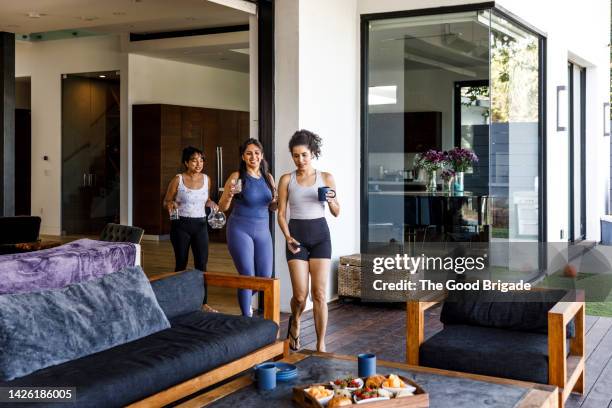 female friends talking with each other while walking towards sofa at villa - athleisure stock pictures, royalty-free photos & images