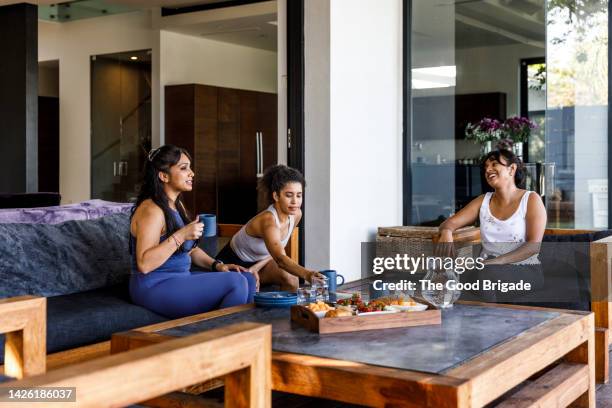 female friends talking with each other while sitting on sofa at villa - athleisure stock pictures, royalty-free photos & images