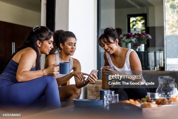 smiling woman sharing smart phone with female friends - athleisure stock pictures, royalty-free photos & images