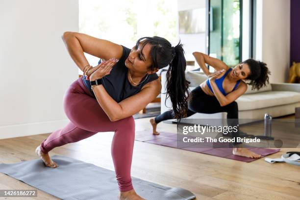 full length of female friends with hands clasped practicing yoga at home - yoga woman fitness stock pictures, royalty-free photos & images
