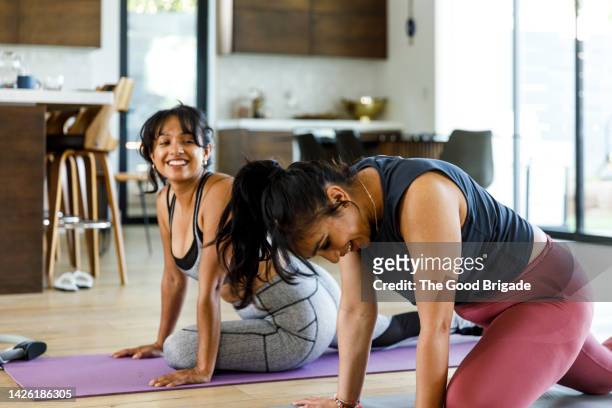 happy woman looking at female friend doing yoga at home - salle yoga photos et images de collection