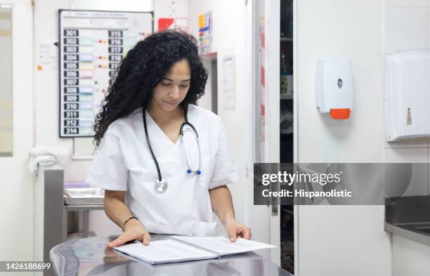 focused nurse at the nurses station looking at a notebook - nursing scrubs stock pictures, royalty-free photos & images