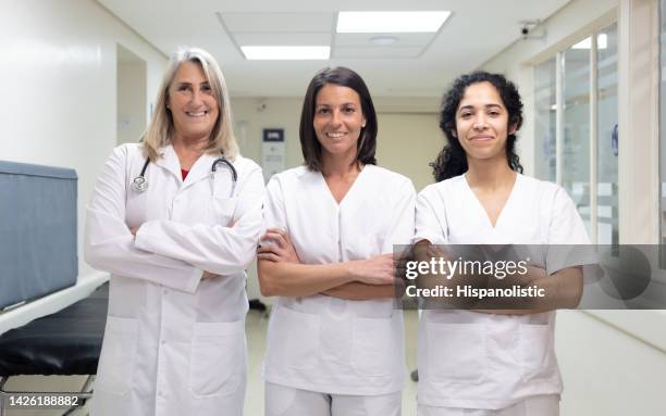 team of female senior doctor and nurses standing at the hospitals corridor facing camera with arms crossed smiling and looking very confident - civilian stock pictures, royalty-free photos & images