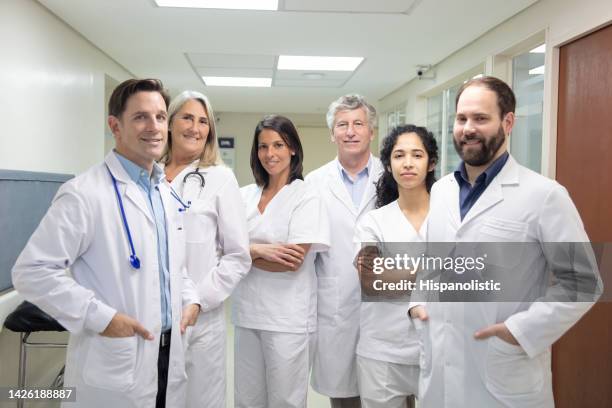 team of doctors and nurses at the hospitals corridor all facing camera smiling - medium group stock pictures, royalty-free photos & images