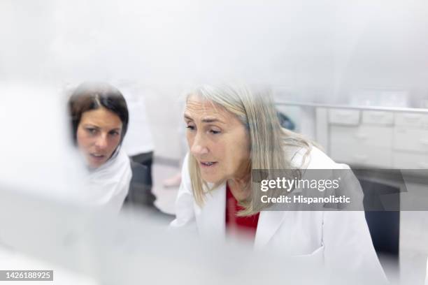 senior female doctor and nurse going over a medical record at the nurses station - doctor scrubs stock pictures, royalty-free photos & images