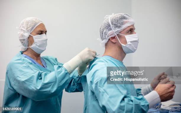 female senior nurse helping male surgeon get ready for a surgery - biosecurity stock pictures, royalty-free photos & images