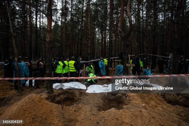 Forensic technicians stand near white body bags at the site of a mass burial in a forest during exhumation on September 16, 2022 in Izium, Ukraine....