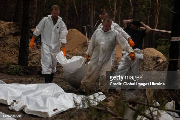 Forensic technicians carry a white body bag at the site of a mass burial in a forest during exhumation on September 16, 2022 in Izium, Ukraine....