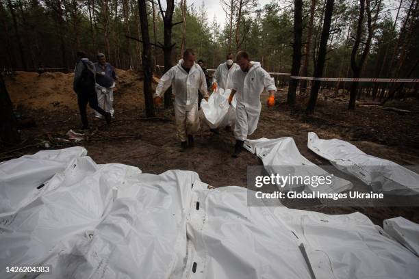 Forensic technicians carry a white body bag at the site of a mass burial in a forest during exhumation on September 16, 2022 in Izium, Ukraine....