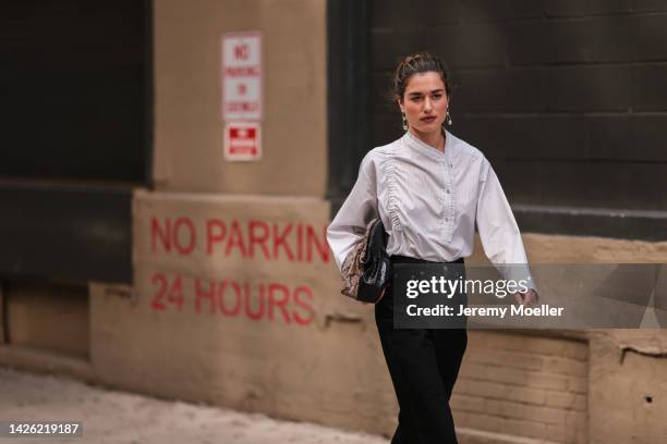 Guest is seen wearing silver earrings, white ruffled button shirt, black/brown leather pattern clutch bag and a black denim jeans pants, outside COS,...