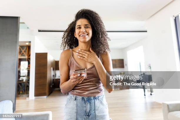 happy woman with curly hair holding mobile phone at vacation home - relief emotion fotografías e imágenes de stock