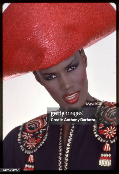 Portrait of Jamaican-born model, singer, and actress Grace Jones as she wears a bright red hat and multi-colored top, New York, New York, late...