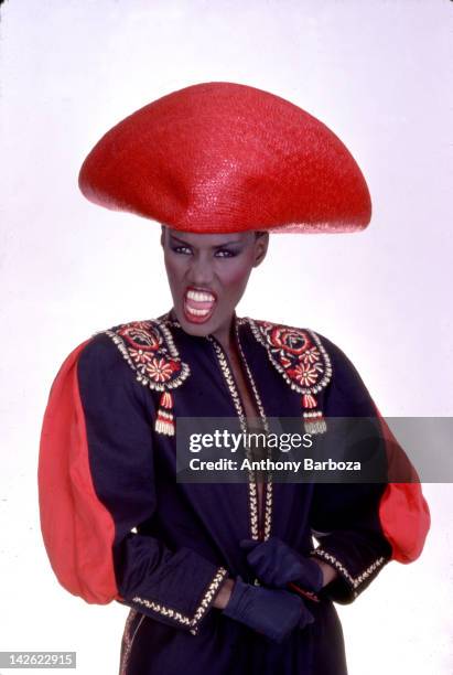 Portrait of Jamaican-born model, singer, and actress Grace Jones as she wears a bright red hat and multi-colored top, New York, New York, late...