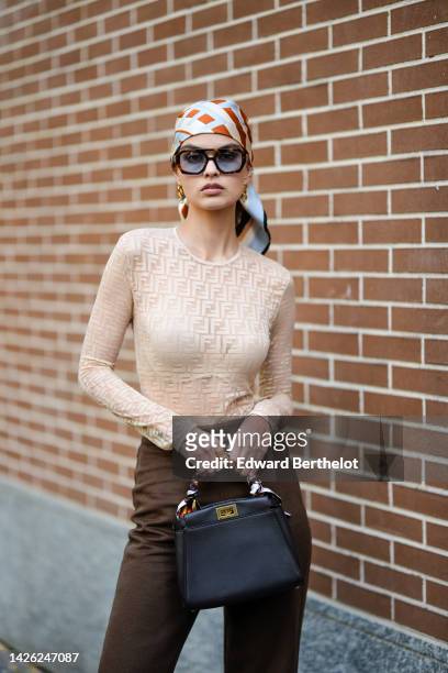 Guest wears a beige and camel striped print pattern silk scarf as a headband, sunglasses, a beige FF monogram print pattern tulle / long sleeves...
