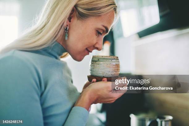 a beautiful woman sniffs the aroma of coffee at home - odorat photos et images de collection