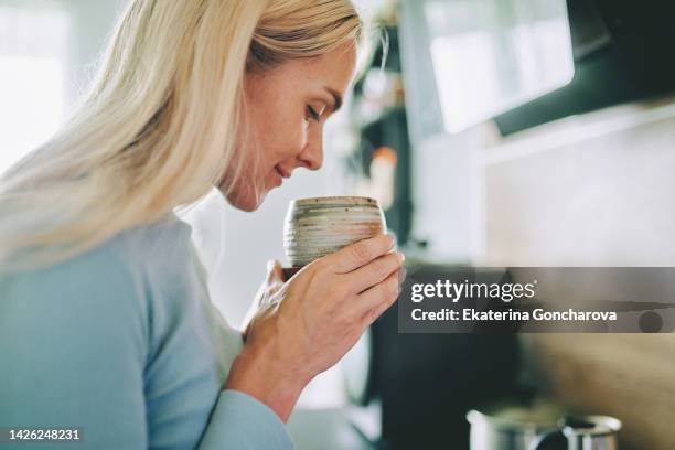 a beautiful woman sniffs the aroma of coffee at home - odorat photos et images de collection
