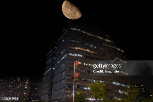 the moon rises over modern buildings - half moon position stock pictures, royalty-free photos & images