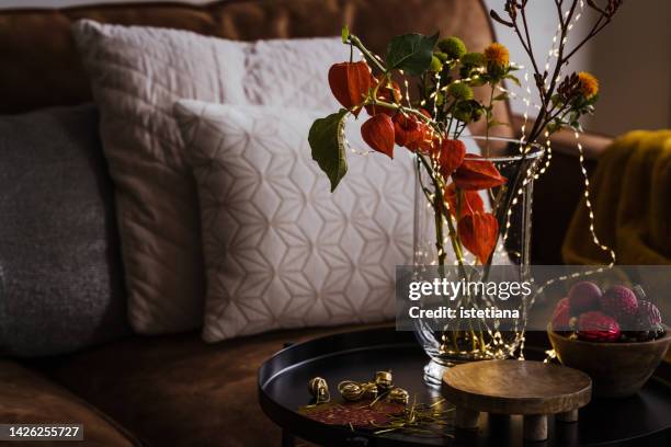 still life of christmas home decor with vase, green and orange flowers, lights, christmas ornaments - christmas still life stock-fotos und bilder