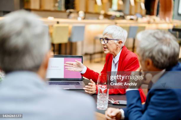 senior businesswoman giving a presentation on her laptop to the others at her table. - dining presentation food stock pictures, royalty-free photos & images